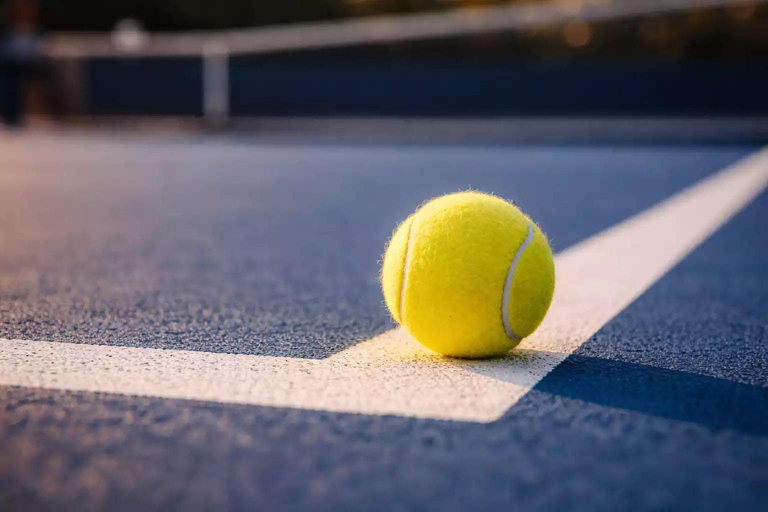 Tennisball auf der Linie eines Hartplatzes mit verschwommenem Netz